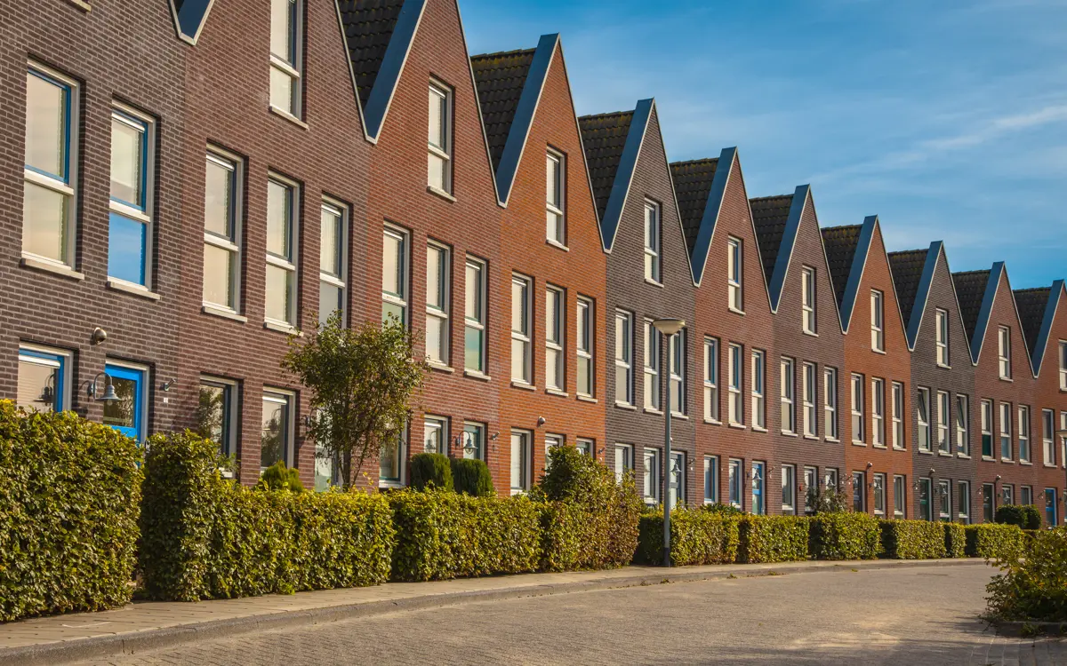 Een rij nieuwbouwwoningen met veel groene struiken in de tuin.