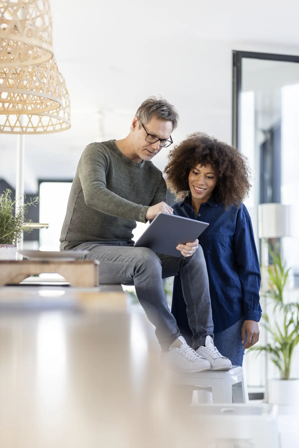 Stel kijken lachend samen naar een tablet. De man zit en de vrouw staat.