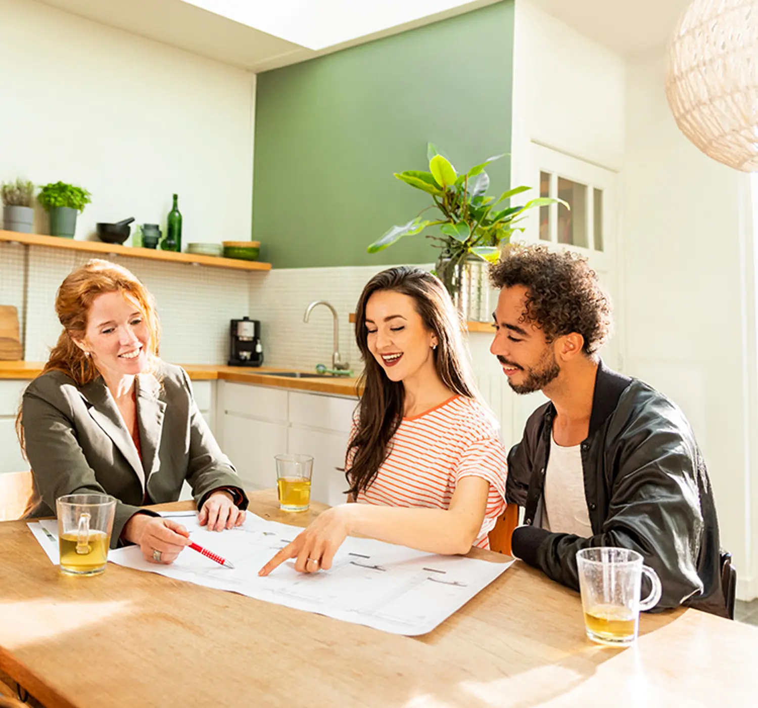 Adviseur zit met klanten aan de keukentafel. De adviseur wijst iets aan op een document.