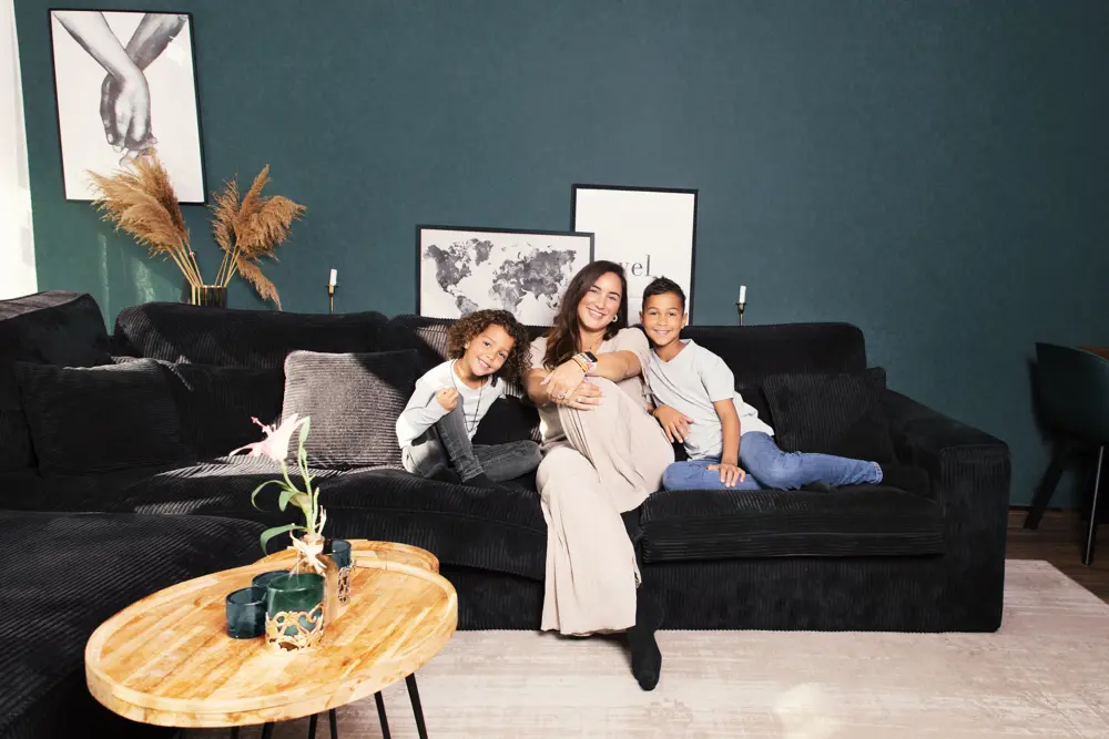 Moeder met twee kinderen zitten met opgetrokken benen gezellig op de bank in de woonkamer.